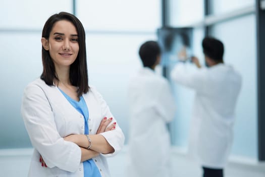 Young smiling woman-doctor is standing with arms crossed in a clinic office.