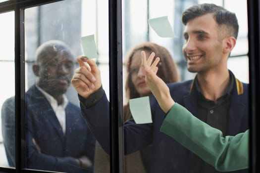 Creative business team looking at sticky notes on glass window