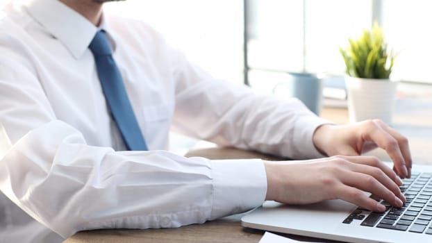 A businessman man in close-up in a shirt is typing on a laptop.