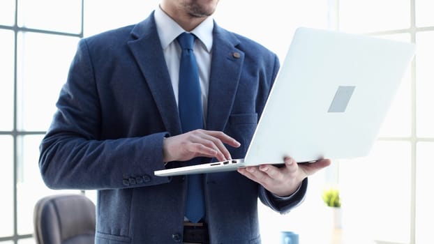 A male businessman in a close-up in a jacket uses a laptop.