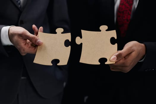 Close-up Of Business Partners Combining Two White Puzzle Pieces On Black Background