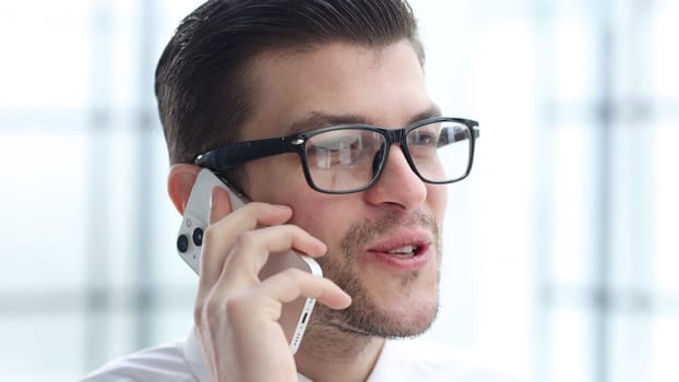 A businessman man in close-up in the office talking on the phone.
