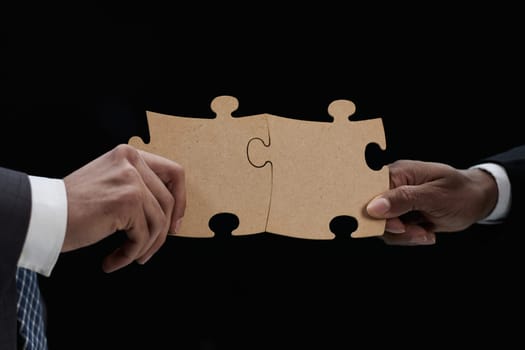 Close-up Of Business Partners Combining Two White Puzzle Pieces On Black Background