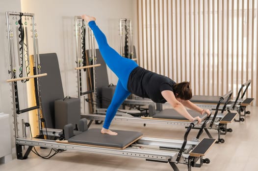 Overweight caucasian woman doing pilates exercises on a reformer