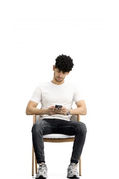 A man, on a white background, is sitting on a chair, with phone.