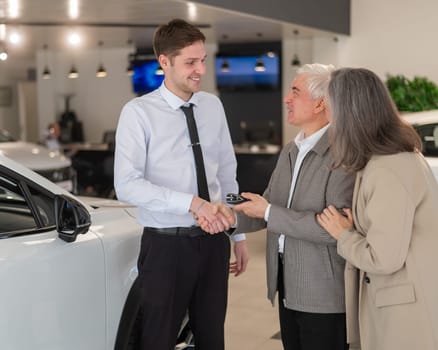 A salesman hands over the keys to a new car to an elderly Caucasian couple