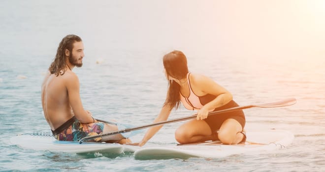 Sea woman and man on sup. Silhouette of happy young woman and man, surfing on SUP board, confident paddling through water surface. Idyllic sunset. Active lifestyle at sea or river