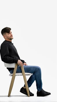 A man, on a white background, sitting on a chair.