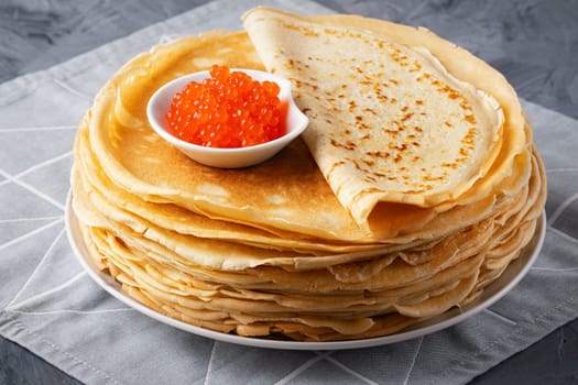 Pancakes with red caviar on grey background.