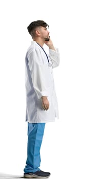 The doctor, in full height, on a white background, talking on the phone.