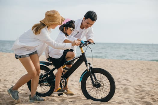A picturesque sunset scene on sandy beach as parents teach their children joy of bicycle riding during summer road trip. Smiles balance and carefree happiness define this memorable family moment.