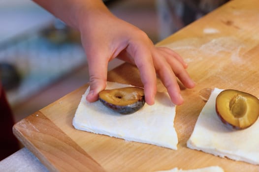 Preparation of homemade fruit dumplings with plums. Czech specialty of sweet good food. Dough on kitchen wooden table with hands.