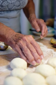 Preparation of homemade fruit dumplings with plums. Czech specialty of sweet good food. Dough on kitchen wooden table with hands.