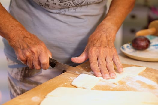 Preparation of homemade fruit dumplings with plums. Czech specialty of sweet good food. Dough on kitchen wooden table with hands.