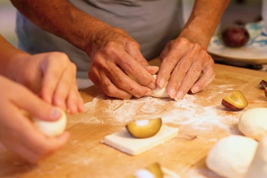 Preparation of homemade fruit dumplings with plums. Czech specialty of sweet good food. Dough on kitchen wooden table with hands.