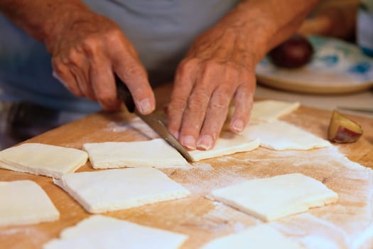 Preparation of homemade fruit dumplings with plums. Czech specialty of sweet good food. Dough on kitchen wooden table with hands.