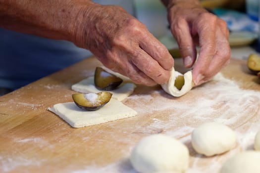 Preparation of homemade fruit dumplings with plums. Czech specialty of sweet good food. Dough on kitchen wooden table with hands.