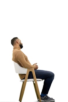 A man, full-length, on a white background, sitting on a chair.