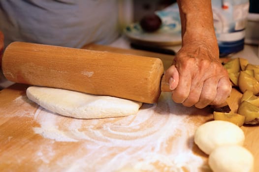 Preparation of homemade fruit dumplings with plums. Czech specialty of sweet good food. Dough on kitchen wooden table with hands.