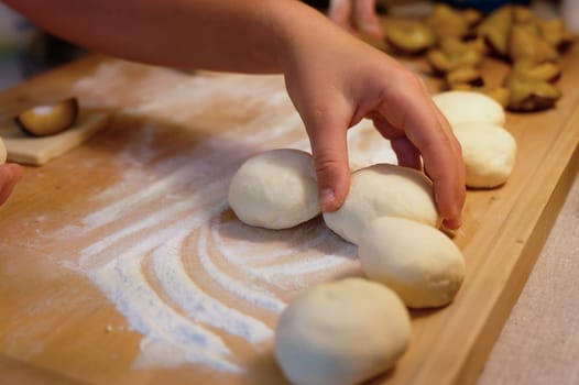 Preparation of homemade fruit dumplings with plums. Czech specialty of sweet good food. Dough on kitchen wooden table with hands.