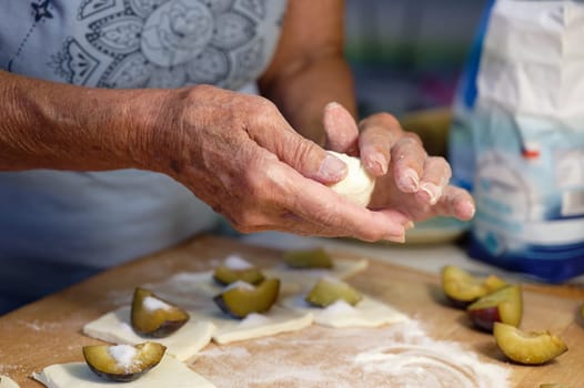 Preparation of homemade fruit dumplings with plums. Czech specialty of sweet good food. Dough on kitchen wooden table with hands.