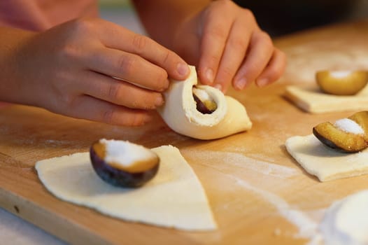 Preparation of homemade fruit dumplings with plums. Czech specialty of sweet good food. Dough on kitchen wooden table with hands.