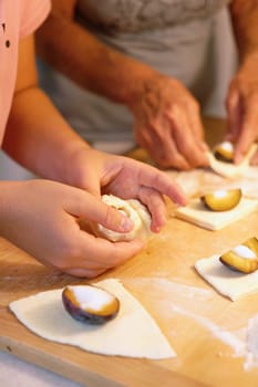 Preparation of homemade fruit dumplings with plums. Czech specialty of sweet good food. Dough on kitchen wooden table with hands.