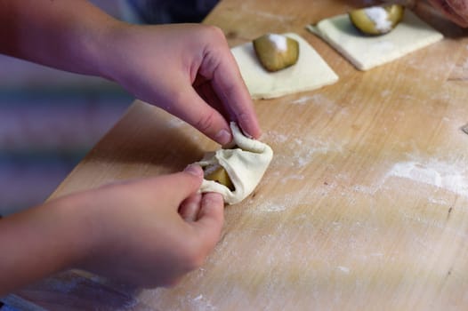 Preparation of homemade fruit dumplings with plums. Czech specialty of sweet good food. Dough on kitchen wooden table with hands.