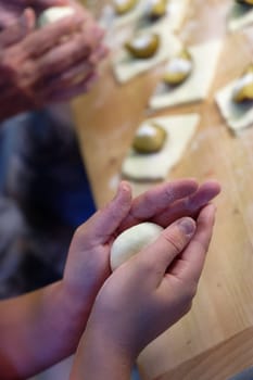 Preparation of homemade fruit dumplings with plums. Czech specialty of sweet good food. Dough on kitchen wooden table with hands.