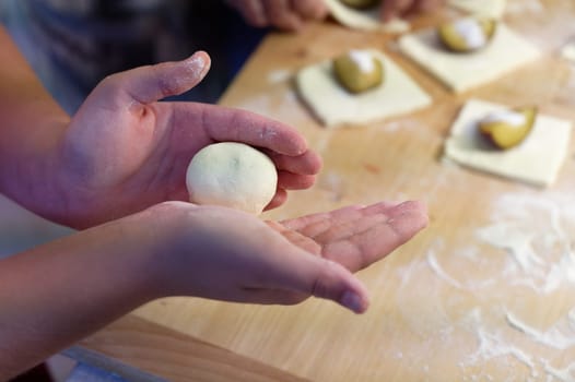 Preparation of homemade fruit dumplings with plums. Czech specialty of sweet good food. Dough on kitchen wooden table with hands.