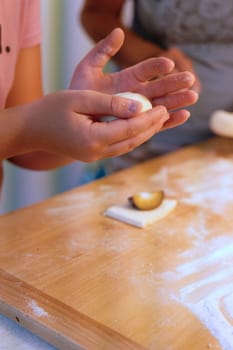 Preparation of homemade fruit dumplings with plums. Czech specialty of sweet good food. Dough on kitchen wooden table with hands.