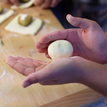 Preparation of homemade fruit dumplings with plums. Czech specialty of sweet good food. Dough on kitchen wooden table with hands.