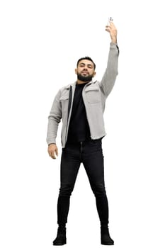 A man, full-length, on a white background, waving his phone.