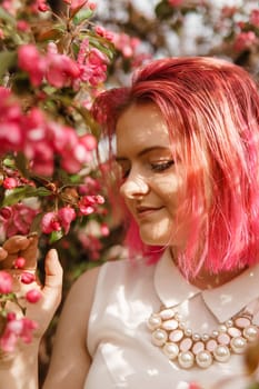 Young girl with pink hair in an Apple orchard. Beautiful young girl in a blooming garden of pink Apple trees.