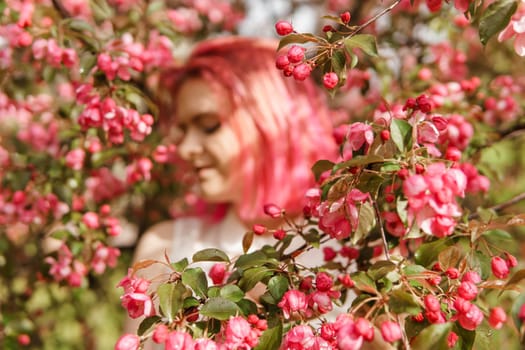 Young girl with pink hair in an Apple orchard. Beautiful young girl in a blooming garden of pink Apple trees.