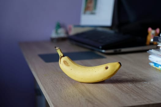 A beautiful fresh banana on a work table at home or in the office with a computer or laptop - notebook.