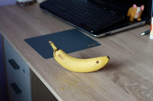 A beautiful fresh banana on a work table at home or in the office with a computer or laptop - notebook.