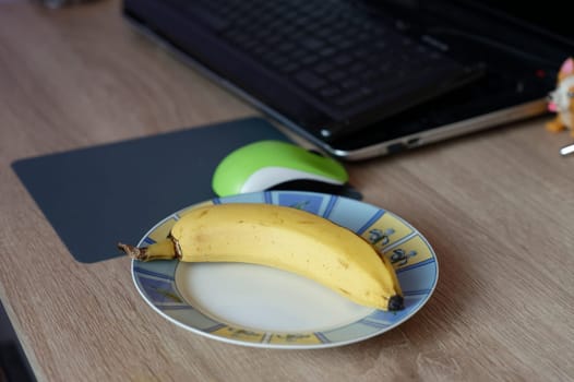 A beautiful fresh banana on a work table at home or in the office with a computer or laptop - notebook.