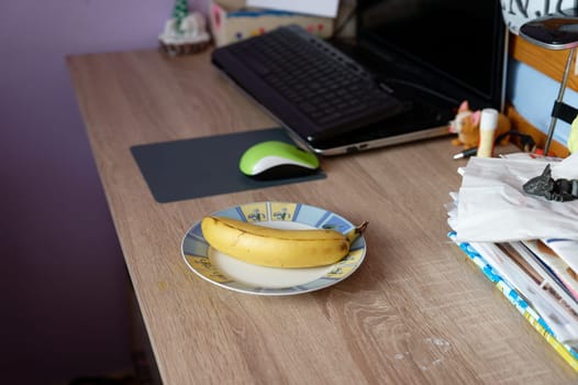 A beautiful fresh banana on a work table at home or in the office with a computer or laptop - notebook.