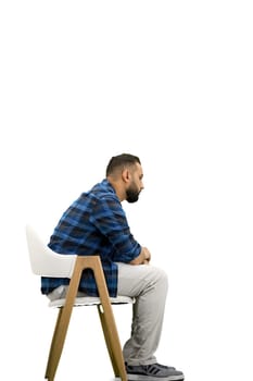 A man, full-length, on a white background, sitting on a chair.