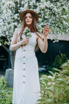 Beautiful young girl in white dress and hat in blooming Apple orchard. Blooming Apple trees with white flowers