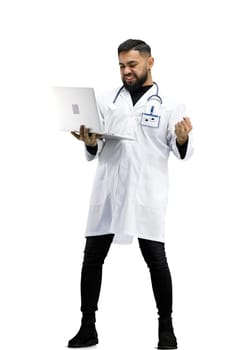 The doctor, in full height, on a white background, uses a laptop.