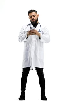 The doctor, in full height, on a white background, uses a phone.