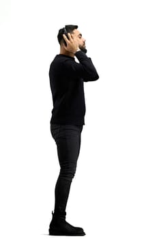 A man, in full height, on a white background, listens to music with headphones.