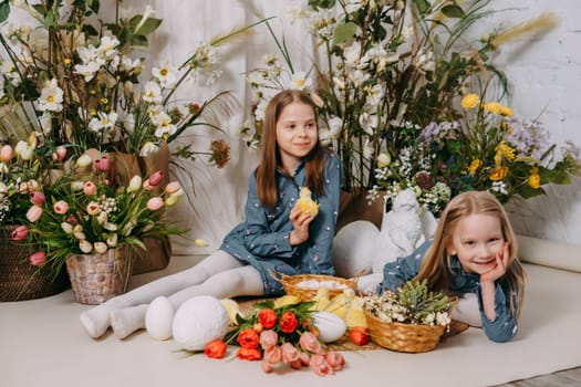 Two girls in a beautiful Easter photo zone with flowers, eggs, chickens and Easter bunnies. Happy Easter holiday