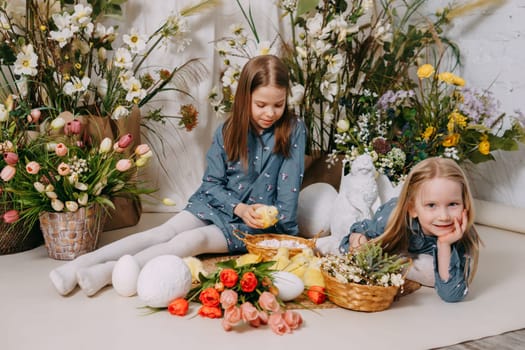 Two girls in a beautiful Easter photo zone with flowers, eggs, chickens and Easter bunnies. Happy Easter holiday