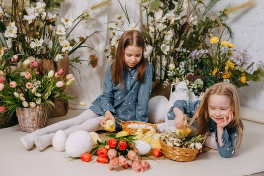 Two girls in a beautiful Easter photo zone with flowers, eggs, chickens and Easter bunnies. Happy Easter holiday