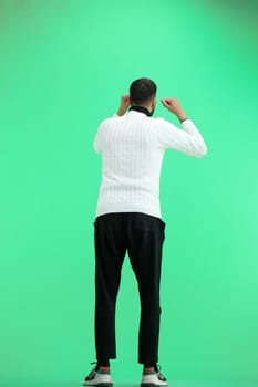 A man, full-length, on a green background, raised his hands up.