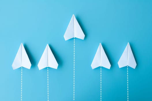 Top view of white paper airplanes origami flying on blue background.