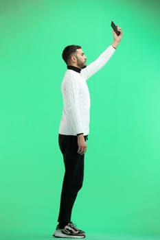 A man, full-length, on a green background, waving his phone.